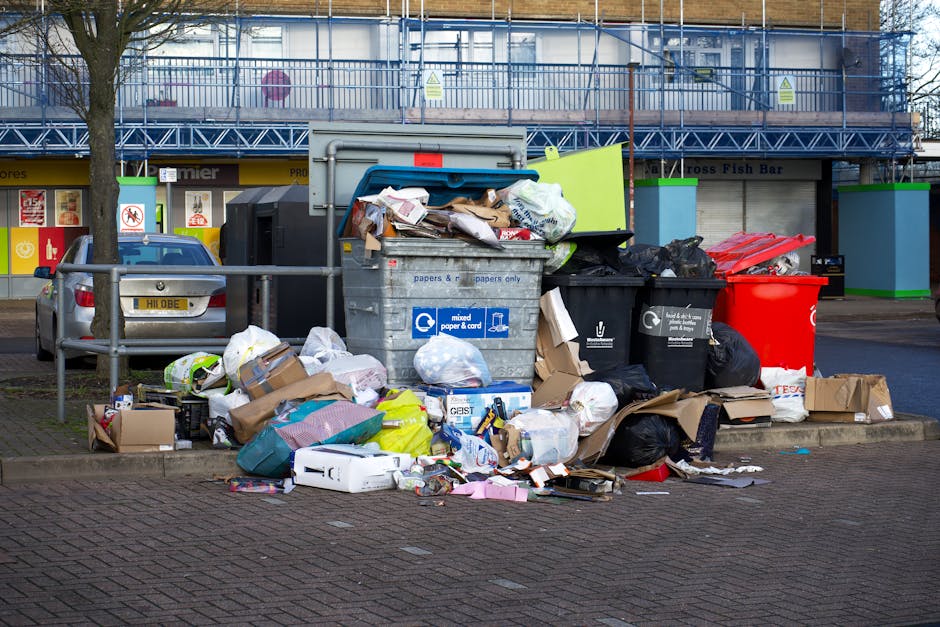 A person with a dark wristwatch on their left wrist is typing on a silver laptop placed on a wooden surface. The laptop's screen displays lines of colorful code with a dark background, indicating codi