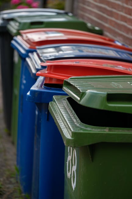 In the foreground, a large collection of mixed household waste is piled on a paved street corner, including open black and black-and-grey bins overflowing with crumpled papers, cardboard boxes, plasti